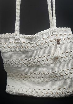 a white crocheted bag hanging on a black background with the bottom part of it's handle