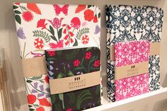 three notebooks are sitting on a shelf with tags attached to them, both decorated in different patterns and colors