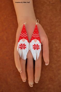 a pair of red and white beaded earrings on someone's hand