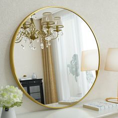 a mirror sitting on top of a white dresser next to a lamp and a vase with flowers