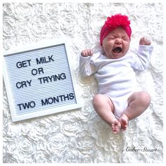 a baby laying next to a sign that says get milk or cry trying two months