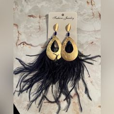 a pair of gold and black earrings with feathers hanging from it's ear hooks