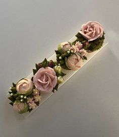 some pink flowers are on top of a white box with green leaves and pearls around it