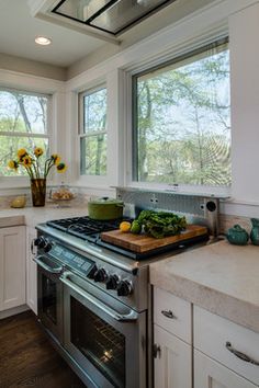 a kitchen with an oven, sink and counter tops in front of two large windows