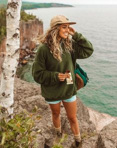 a woman standing on top of a rocky cliff next to the ocean wearing a hat