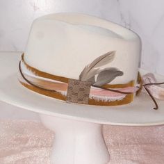 This hatband is gorgeous and has just a little extra added to it. The band is 22.5" x 1.5" and has adjustable ties in the back so it can fit hats from 22.5-34". The bottom layer is one of our favorite leathers, a metallic toasted bronze pink. Very subtle but gorgeous! The designer has then used two types of silk ribbons that complement the leather and really bring the color to life. The brown suede lace adds a nice complete to complete the top layer. As if that wasn't enough...we have added a sm White Adjustable Fedora With Flat Crown, Adjustable White Fedora With Flat Crown, Adjustable Country Fedora For Kentucky Derby, White Adjustable Hat With Flat Crown, Elegant Adjustable Fedora With Flat Crown, White Adjustable Flat Crown Hat, Adjustable Brimmed Mini Hats For Kentucky Derby, Brown Adjustable Mini Hat With Short Brim, Adjustable White Felt Hat With Flat Brim