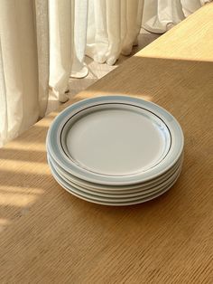 a stack of white plates sitting on top of a wooden table next to a window