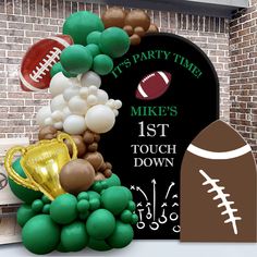 a balloon arch with footballs, balloons and a trophy in front of a brick wall