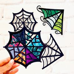 hand holding up stained glass spider webs against a white brick wall