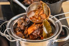 a pot filled with stew and vegetables on top of a stove next to other pots