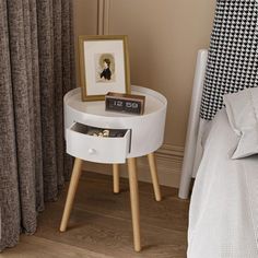 a small white table with an open drawer on it next to a bed and curtains