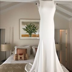 a white wedding dress hanging on a hanger in front of a bed with pillows