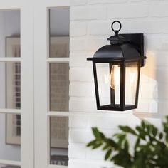 an outdoor light hanging from the side of a white brick wall