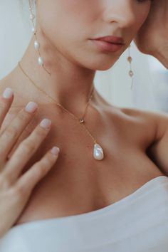 a woman in a white dress is holding her hand up to her face while wearing a pearl necklace