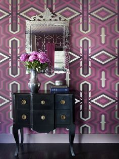 a vase with pink flowers on top of a dresser in front of a mirror and wallpaper