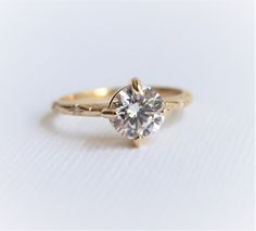 a yellow gold engagement ring with a single diamond in the center on a white background