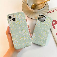 a woman holding two phone cases with daisies on them, next to a cup and saucer