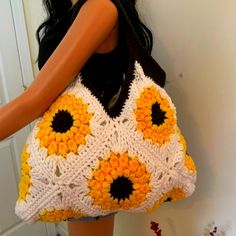 a woman holding a crocheted sunflower purse in front of a white door