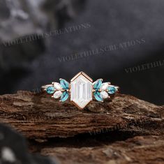 an engagement ring with blue and white stones on top of a tree stump in the woods