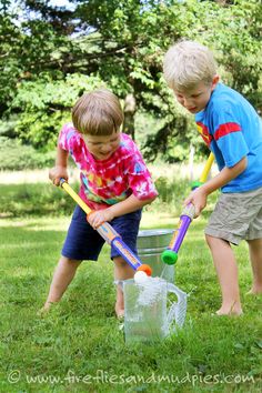 two young boys are playing in the grass with plastic buckets and baseball bats as they stand next to each other