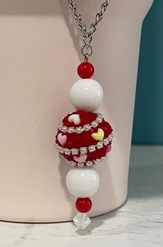 a red and white necklace is hanging from a chain on a vase with a flower in it