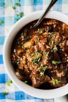 a white bowl filled with meat and gravy on top of a blue checkered table cloth