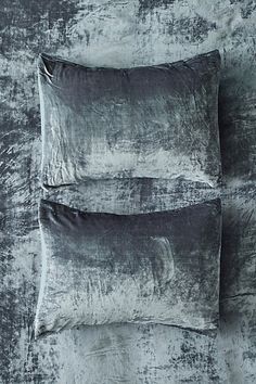 two pillows sitting on top of a bed covered in grey velvets and black sheets