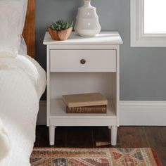 a white nightstand with a book on it next to a bed