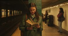 a woman standing next to a train station reading a book