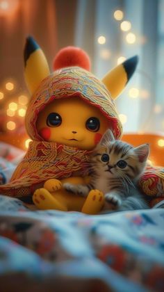 a small kitten sitting next to a stuffed pikachu on top of a bed