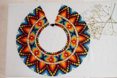 a colorful beaded necklace sitting on top of a table next to a vase with flowers