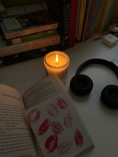 an open book sitting on top of a table next to headphones and a candle