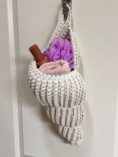 a crocheted basket hanging on a door handle with a purple flower in it