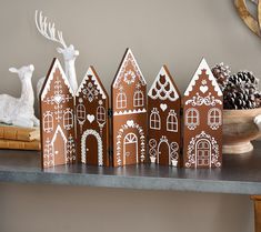 three gingerbread houses sitting on top of a table next to a bowl of pine cones