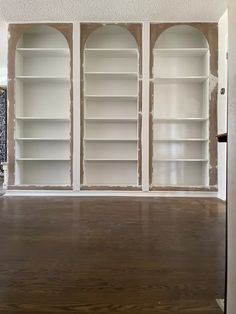 an empty room with white bookcases and wood floors