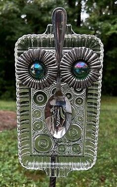 an owl shaped glass object on a stand in the middle of a field with trees and grass