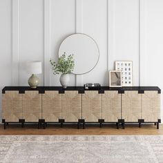 a sideboard with an oval mirror and vases on it in front of a white wall