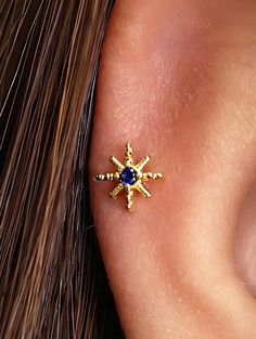 a woman's ear with a star shaped blue stone on the end of it