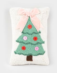 a green christmas tree pillow with buttons and a pink bow on the front, sitting on a white surface