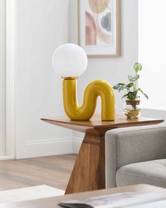 a yellow lamp sitting on top of a wooden table next to a gray chair and potted plant