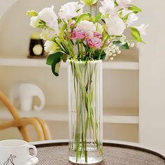 a vase filled with white and pink flowers on top of a table next to a cup