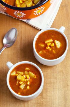 two bowls of soup with corn on the side and a spoon next to it, sitting on a table