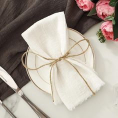 a white plate topped with a napkin next to silverware and pink flowers on top of a table