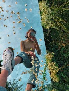 a woman taking a selfie with her cell phone in front of flowers and grass