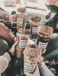 several people holding up cups with coffee and crave toppings on them in the back seat of a car