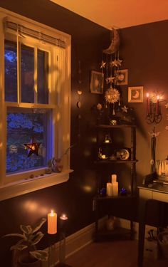 a room with candles and pictures on the wall next to a desk in front of a window