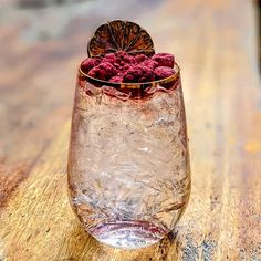 a glass filled with raspberries sitting on top of a wooden table