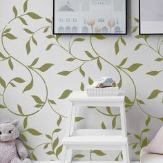 a small white table with a teddy bear on it next to a green leafy wallpaper