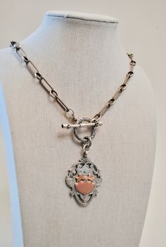 This exquisite Antique English Watch Fob Necklace is a carefully crafted heirloom piece, combining the elegance of sterling silver and the timeless beauty of 9k rose gold. This necklace is attached with a toggle, featuring two garnets. With an English seal embossed on the back of the pendant, this one-of-a-kind necklace is sure to be treasured for generations. Length: 18"Pendant: 1 1/2" Timeless Silver Heart Pendant Jewelry, Engraved Heirloom Metal Jewelry, Classic Heart Pendant Jewelry With Sterling Silver Clasp, Heirloom Silver Heart Pendant Jewelry, Engraved Rose Gold Metal Necklace, Luxury Engraved Rose Gold Jewelry, Luxury Polished Bronze Jewelry, Victorian Sterling Silver Locket Jewelry, Antique Jewelry With Lobster Clasp For Gift