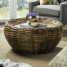 a wicker coffee table with flowers on it in front of a couch and window